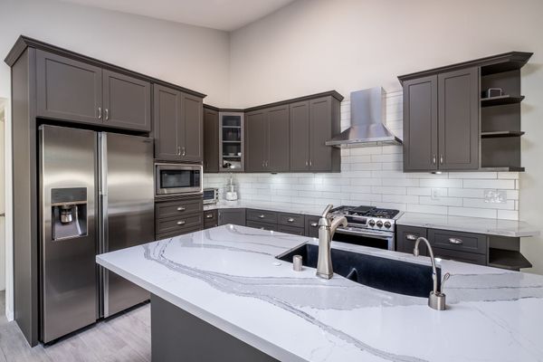 A kitchen with white quartz counters, gray shaker cabinets, stainless appliances and white subway tile backsplash