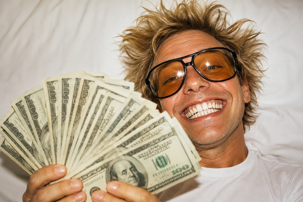 Young man with sunglasses and wild hair showing fanned out hundred dollar bills