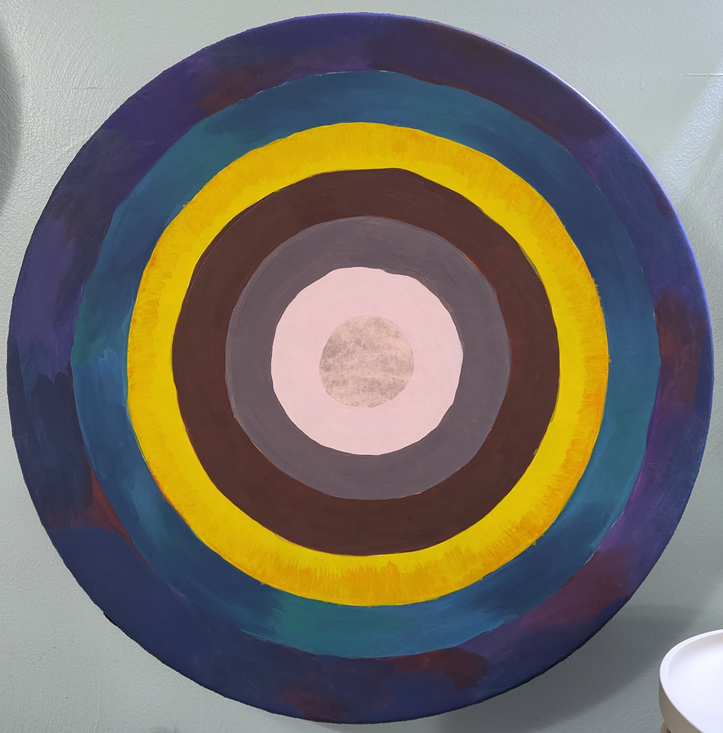 A large hand-drum painted with concentric rings of color. The inner rings are bland white and grey, but the closer you get to the outer rings, the brighter and more varied the colors get.