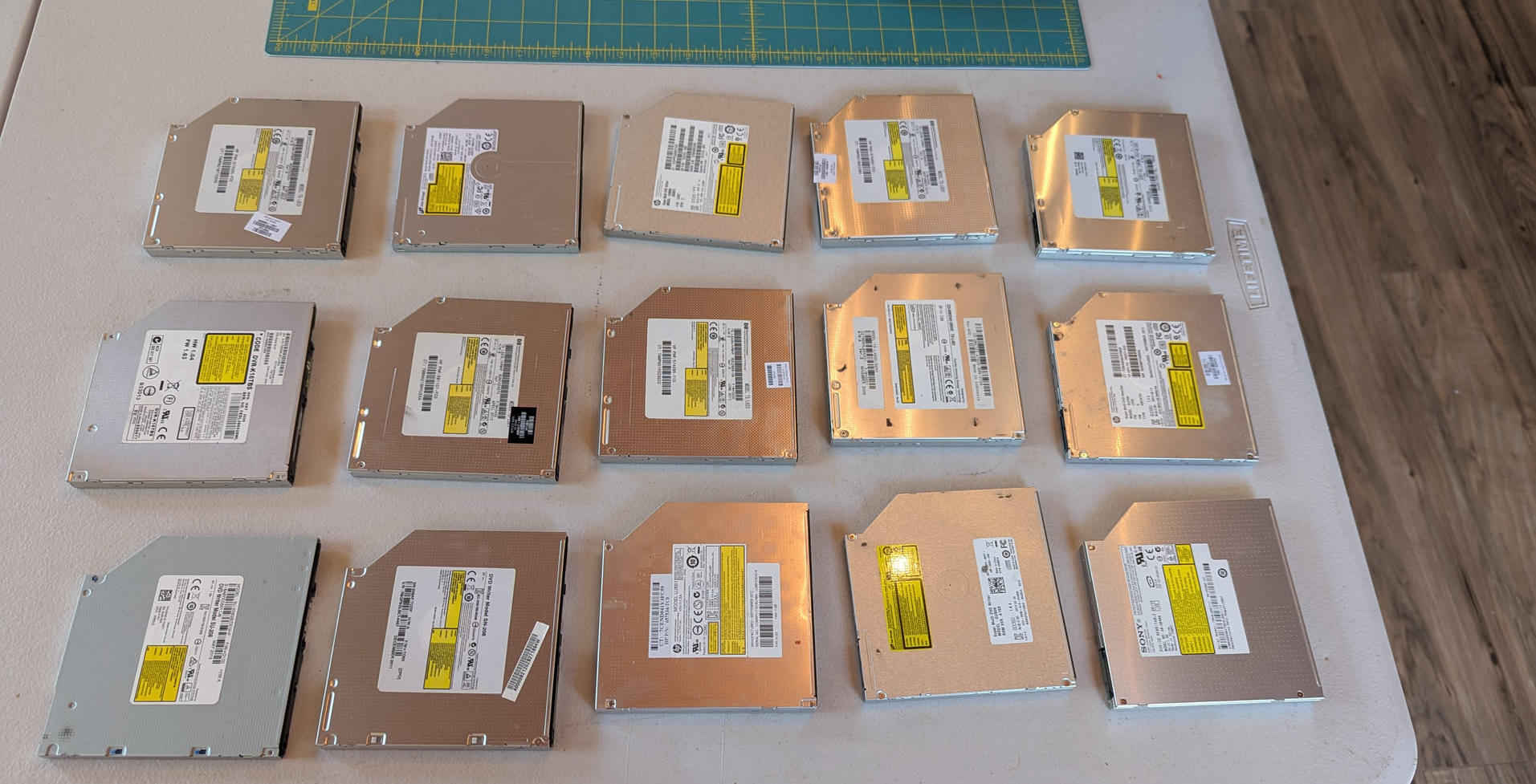 Fifteen laptop optical drives laid out on a table