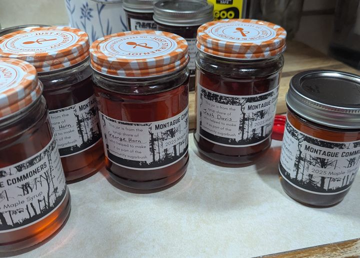 Five jars of syrup sitting on a kitchen countertop. Each jar is labeled with the name of its intended recipient.