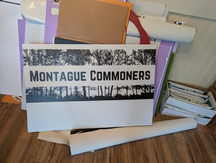 A large version of the Montague Commoners logo printed on a big piece of Coroplast, which is leaning up against a variety of signmaking materials donated by one of our members