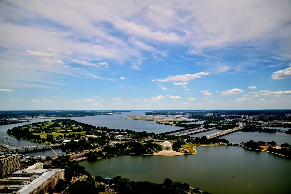The Jefferson Memorial and Reagan National Airport are seen near the center of a photo on aparty sunny day. Much of the ground area is taken up with the Tidal Basin, Potomac River.