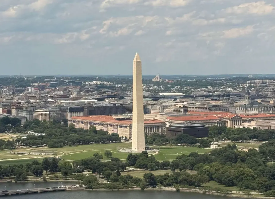 The Washington Monument is seen from a plane on approach to Reagan National Airport. A little of the Tidal Basin is seen at bottom with clouds above.