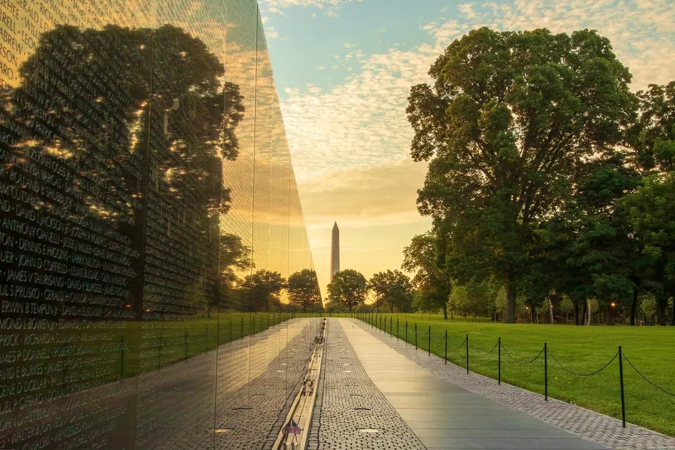 A morning scene reflected in the Vietnam Veterans War Memorial. There are some speckled clouds and Washington Monument.