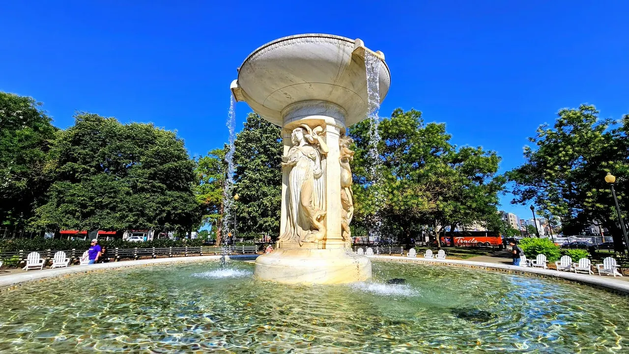 Bright blue skies over the Dupont Circle fountain, which has water coming from it and filling the fountain pool.