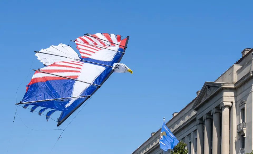 A kite designed like an eagle flies under blue skies near the National Archives.