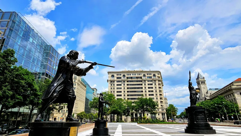 A mix of blue skies and clouds is seen above statues at Freedom Plaza