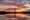 The Washington Monument is seen from the Tidal Basin at sunrise. Clouds are orange and the whole scene glows. 