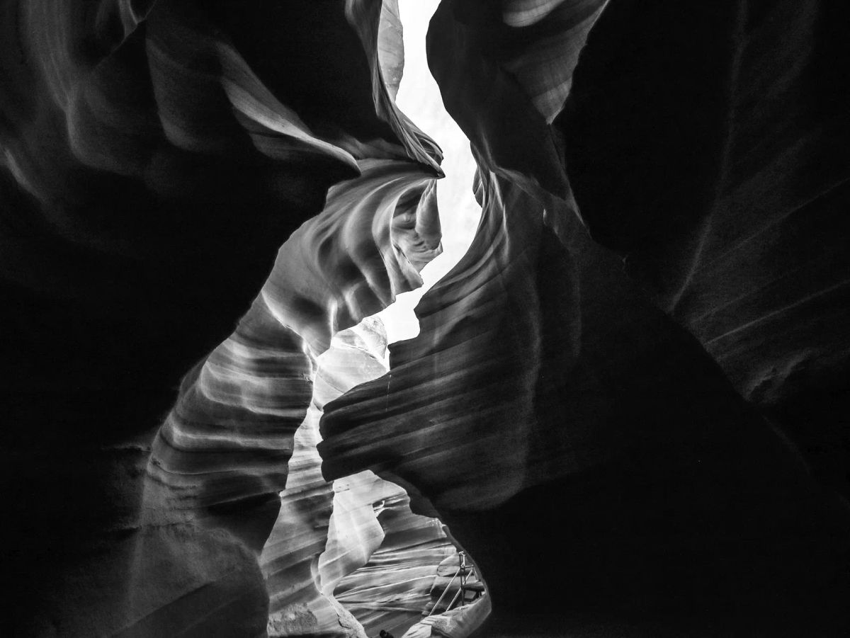 Dramatic b/w photo from inside a dark cavern with dramatically curved/eroded cliffs enclosing a sinuous patch of sky