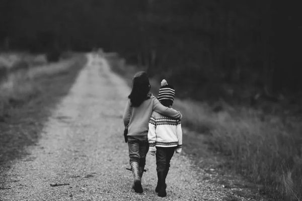 BW pic of two youths from the back bundled in cold-weather gear walking down a dirt path into a blurry distance
