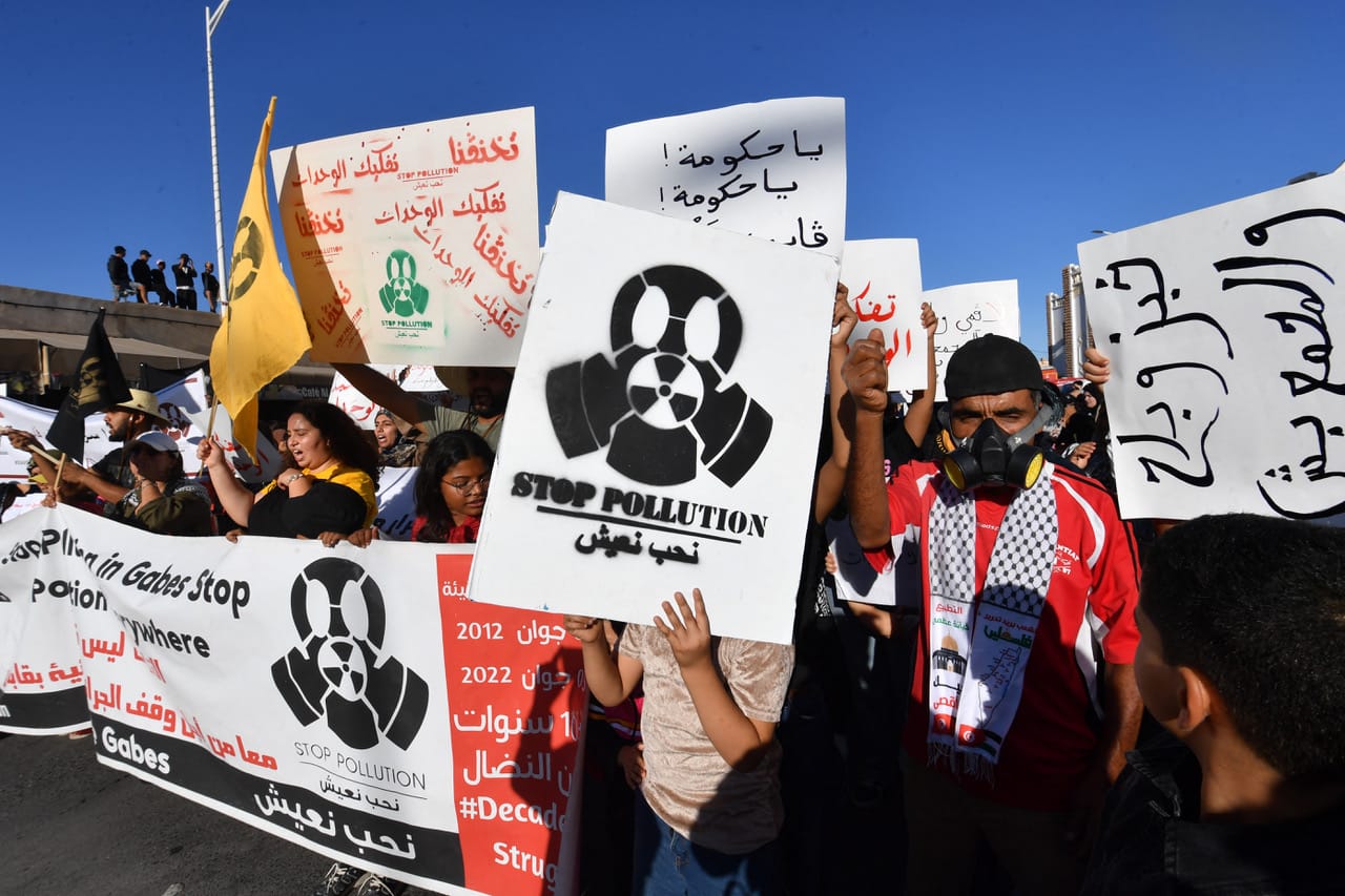 The head of a protest march with signs in Arabic and English featuring screenprints of figures in gas masks. 