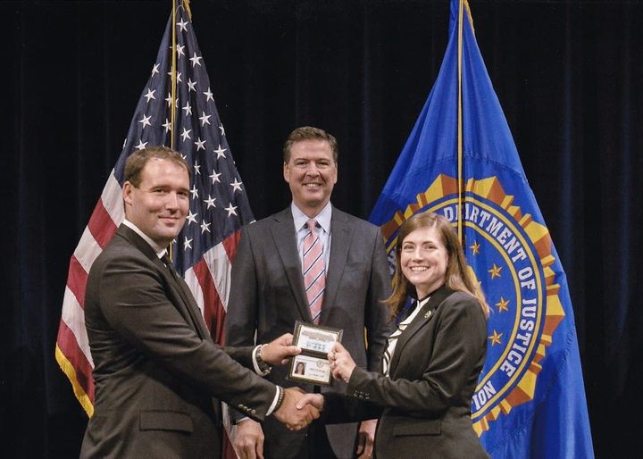 A photograph of Philip presenting Jill with her FBI credential while FBI Director James Comey presides. (July 2016)