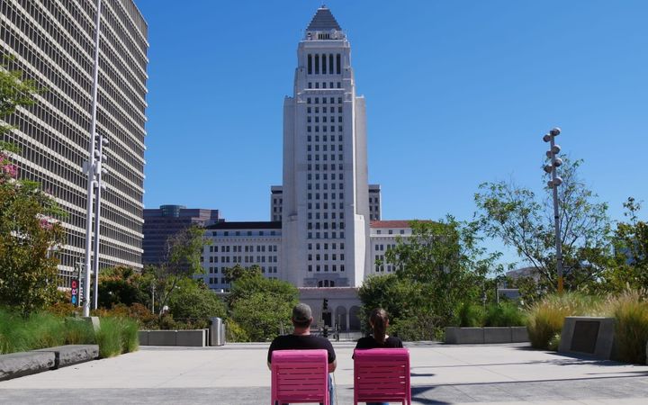 A photo of two people sitting in pink lawn chairs, backs to the camera, with a government building in the distance.