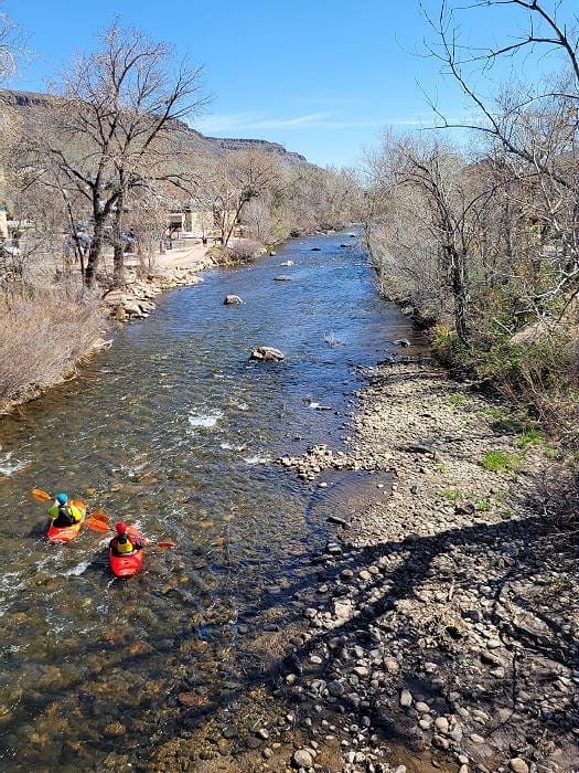 Looking east on Clear Creek in Golden Colorado. Two kayakers are padding in very clear, shallow water.