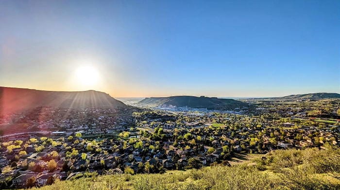 View across the Golden valley with the sun low in the eastern sky. Both Table Mountains appear in the distance and houses fill the mid-ground.