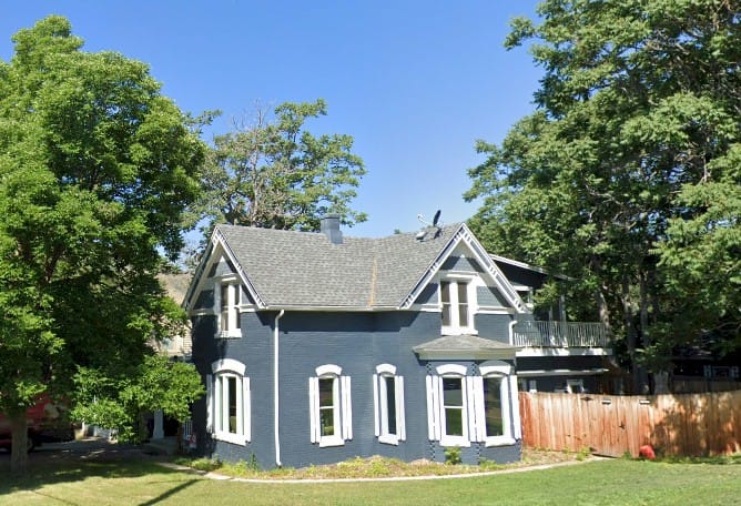 2 story brick Victorian house painted grayish-blue with white shutters