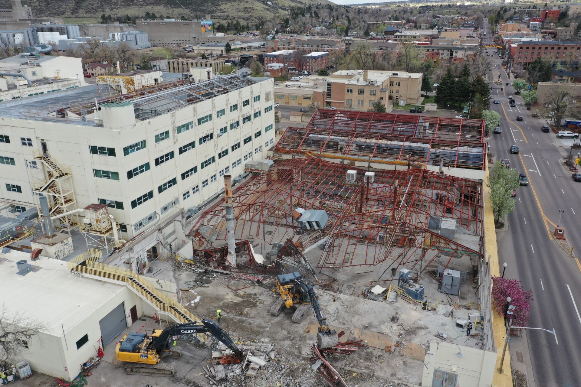 aerial photo of a very large building with steel roof rafters being pulled down by heavy equipment