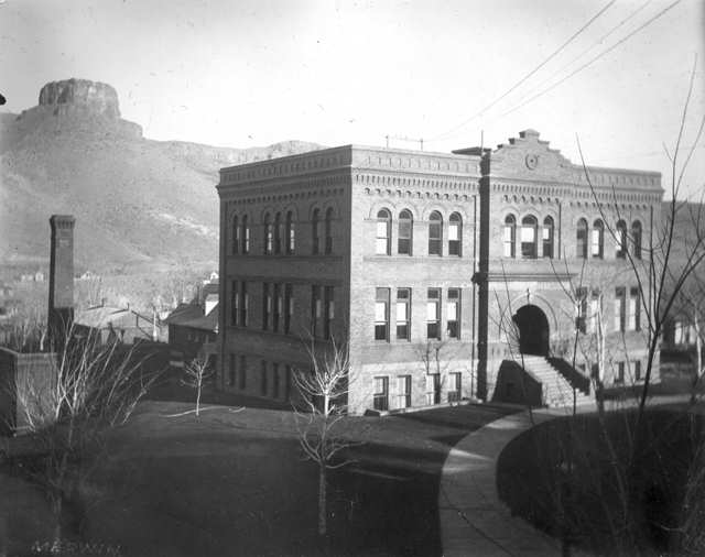 2-1/2 story brick building with central stone stairbase and arched doorway - Castle Rock in background