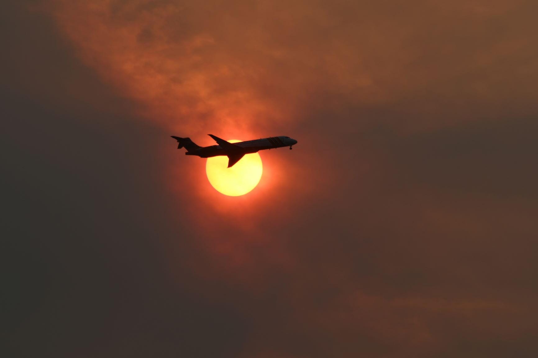 airplane silhouetted against a dark yellow sun in a red-black sky