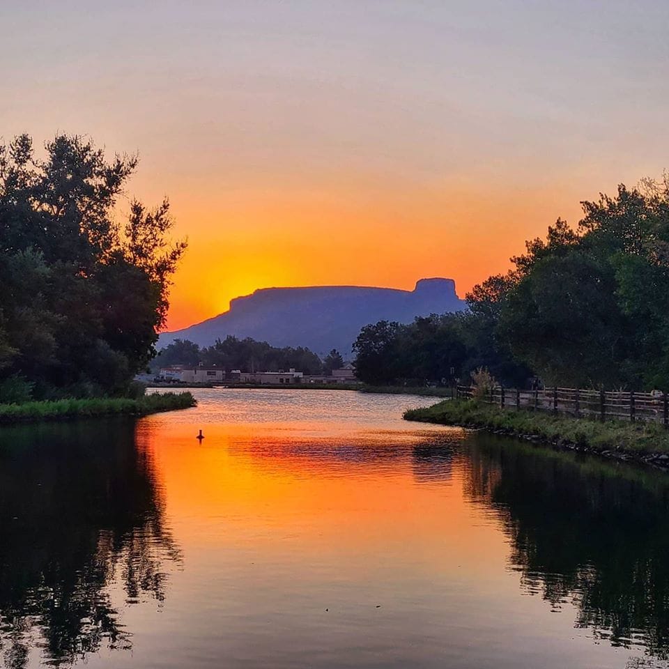 view from the west side of the retention pond silhouette of Castle Rock in the distance and red-orange staining both sky and water