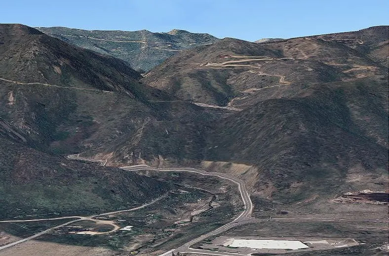 Two-lane paved road heading into the mountains.  Higher up, older, unpaved switchback roads are visible.