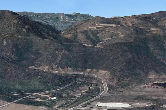 Two-lane paved road heading into the mountains.  Higher up, older, unpaved switchback roads are visible.