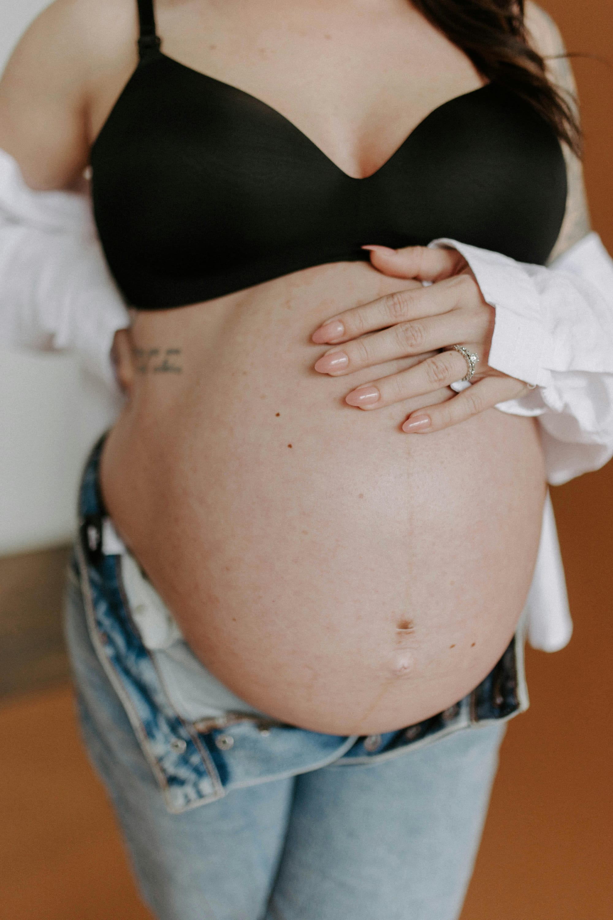 Pregnant woman in button down shirt and bra with hand on belly
