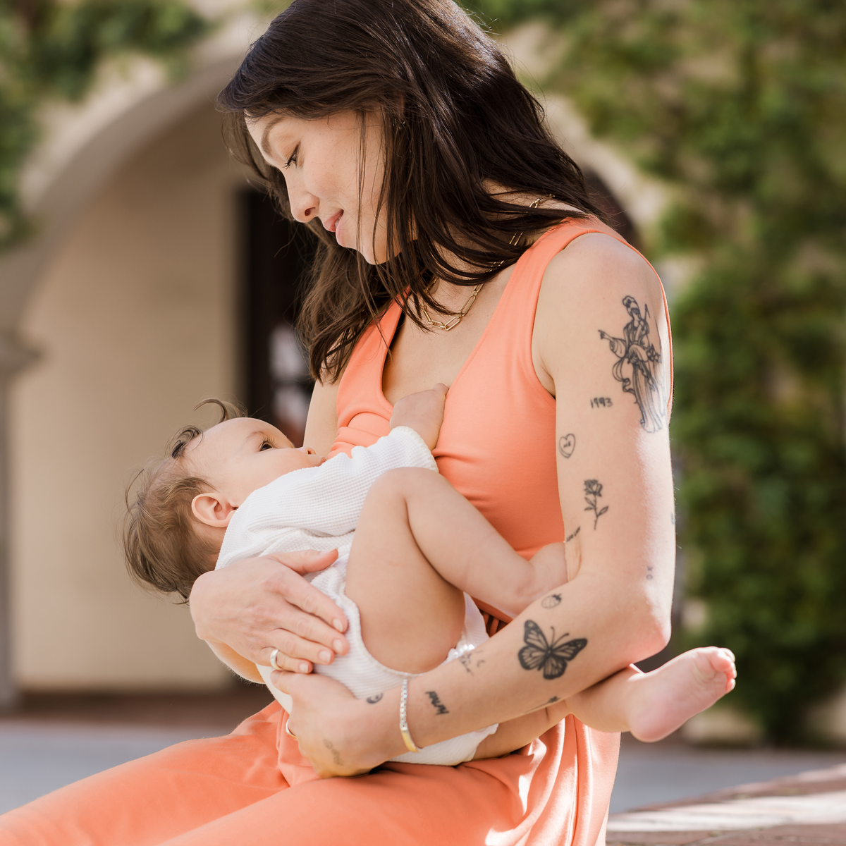 A woman breastfeeding her baby in an orange midi-length nursing dress.