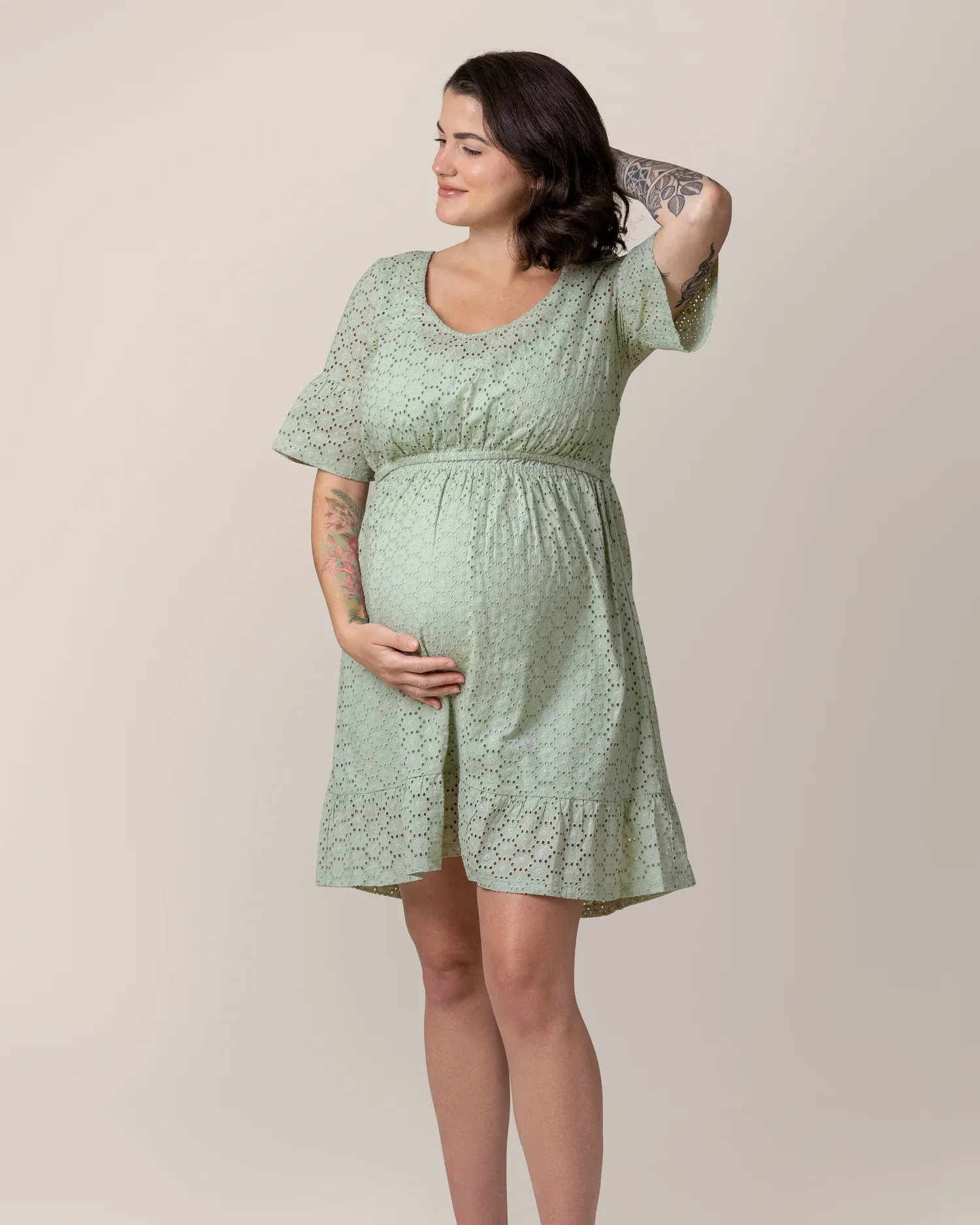 A woman holding her baby bump in the green Dahlia Eyelet Maternity & Nursing Dress by Kindred Bravely.