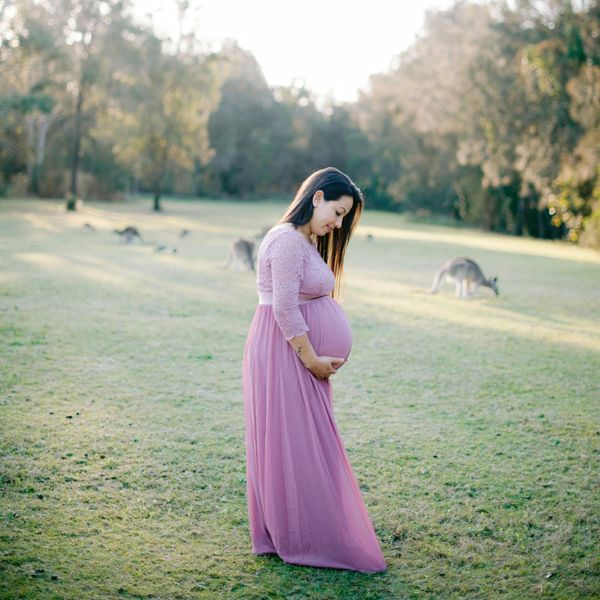 A pregnant woman in a pink maternity dress in a field.