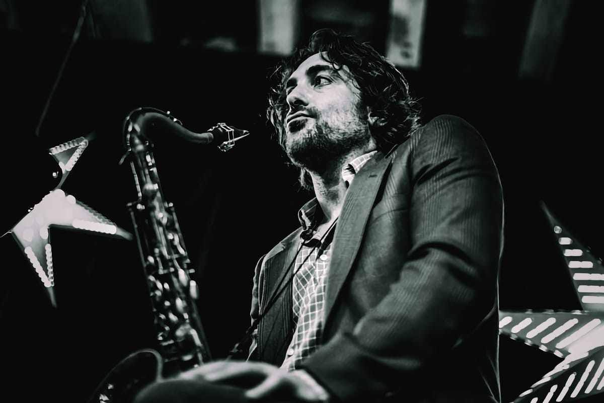 A black-and-white photograph of Noah Preminger at a gig holding his saxophone.
