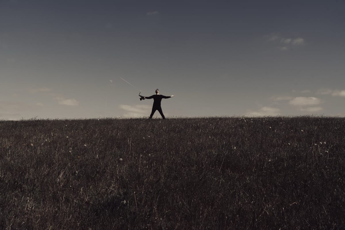 Donny McCaslin standing in a field in the distance, arms outstretched, saxophone in hand - Photo by Dave Stapleton