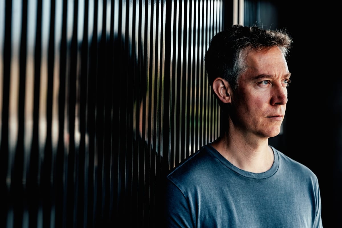 Kodomo in profile view wearing blue shirt against striped backdrop with dramatic side lighting.