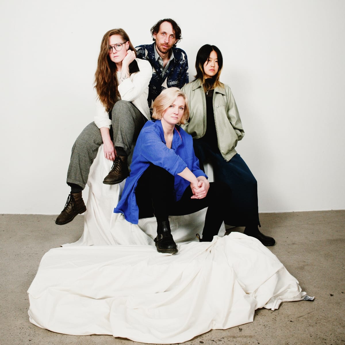 Four members of Bellbird arranged on white-draped furniture, varied clothing including blue shirt and patterned jacket, light background. Photo by Marc Etienne Mongrain.