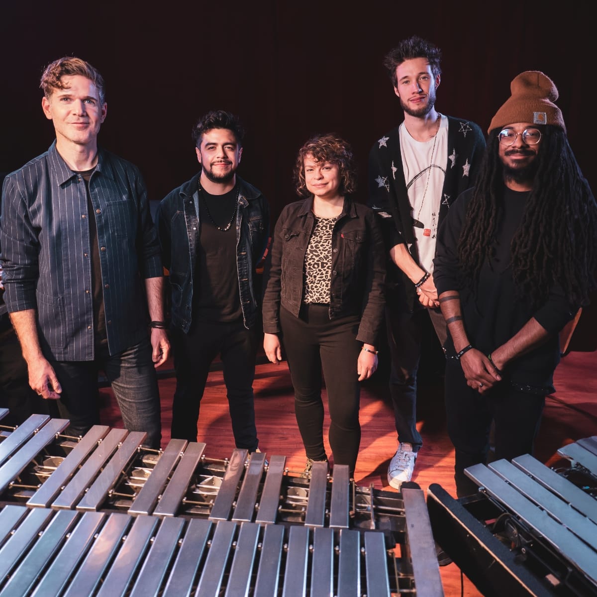 Ben Wendel and his BaRcoDe ensemble pose on a warmly lit stage behind a vibraphone, five musicians in casual dress against a dark background. Photo by Gilad Hekselman.