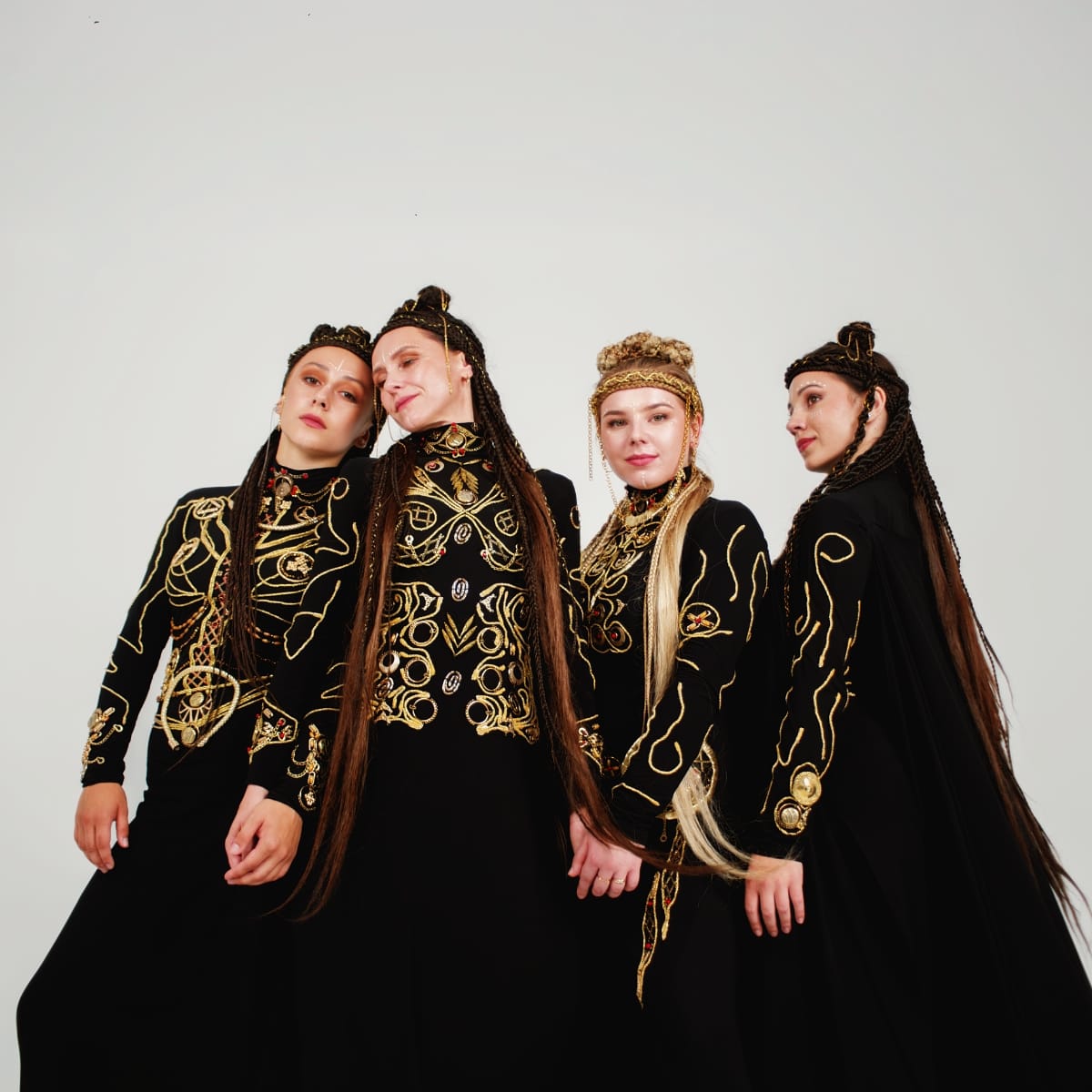 Four members of Ukrainian vocal group YAGÓDY pose in elaborate black garments with gold embroidery and long braided hair with ornate headpieces, against a white background.