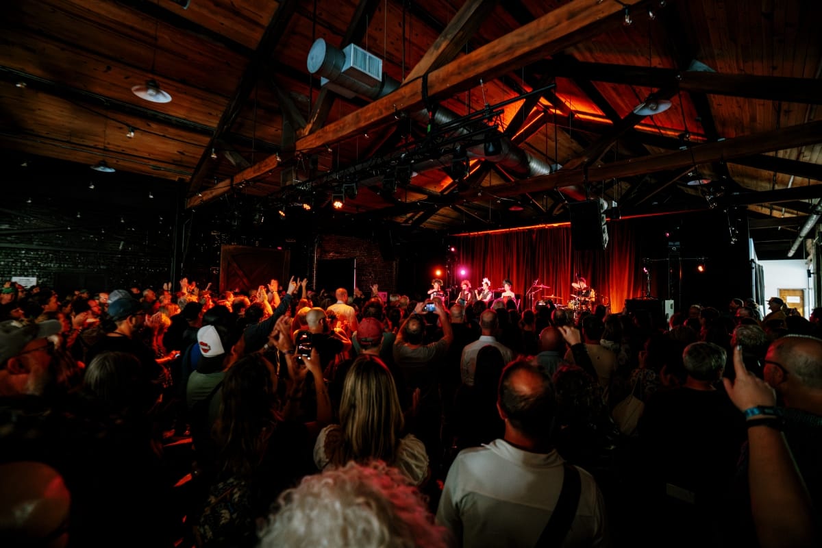 YAGÓDY perform on a red-curtained stage before a packed crowd in a wood-beamed venue, with hands raised throughout the audience, at Big Ears 2026. Photo by Billie Wheeler.