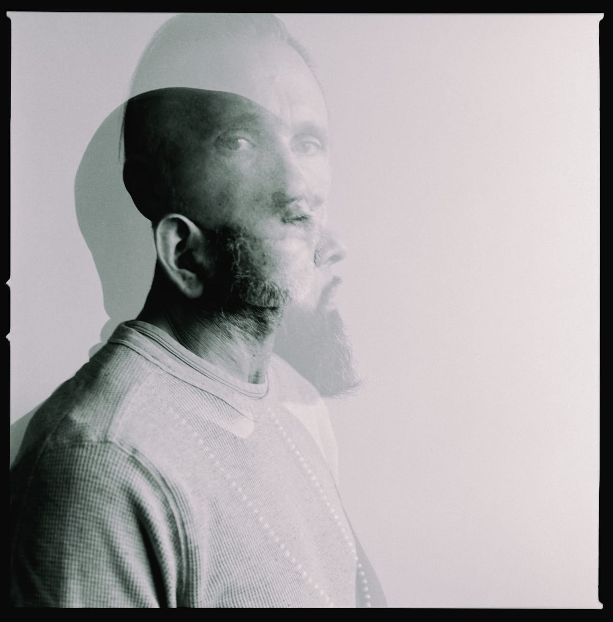 A black-and-white double-exposure portrait of Dälek, two faces overlapping against a pale background, one sharply defined and one ghosted behind. Photo by Ashkan Sahihi.