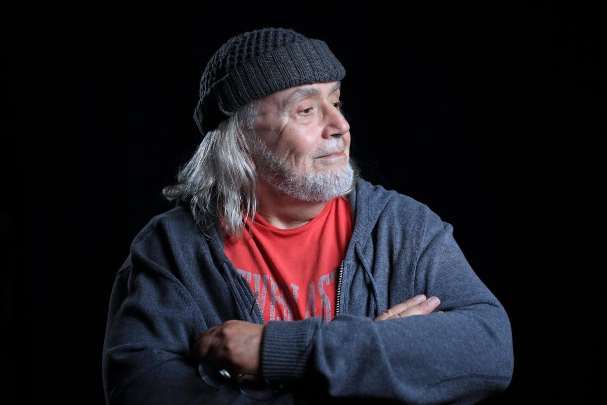 Robert Margouleff, arms crossed, gazes off-camera against a black background, lit from the side.