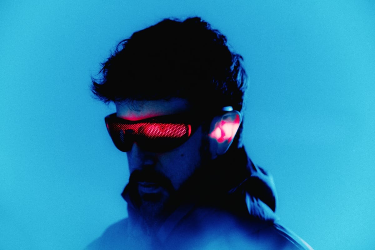 Danalogue seen from the side in a red-glowing wraparound visor, his hair and beard silhouetted against a saturated blue background.
