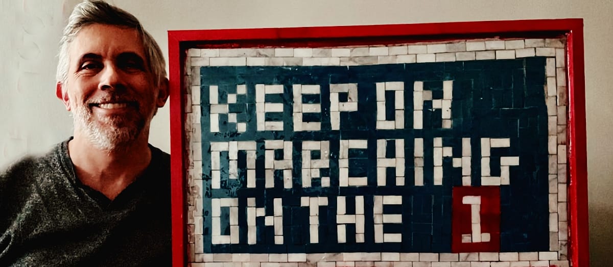 Chris Molanphy smiles beside a red-framed subway-tile mosaic reading "Keep on marching on the 1," the numeral set in a red tile block.