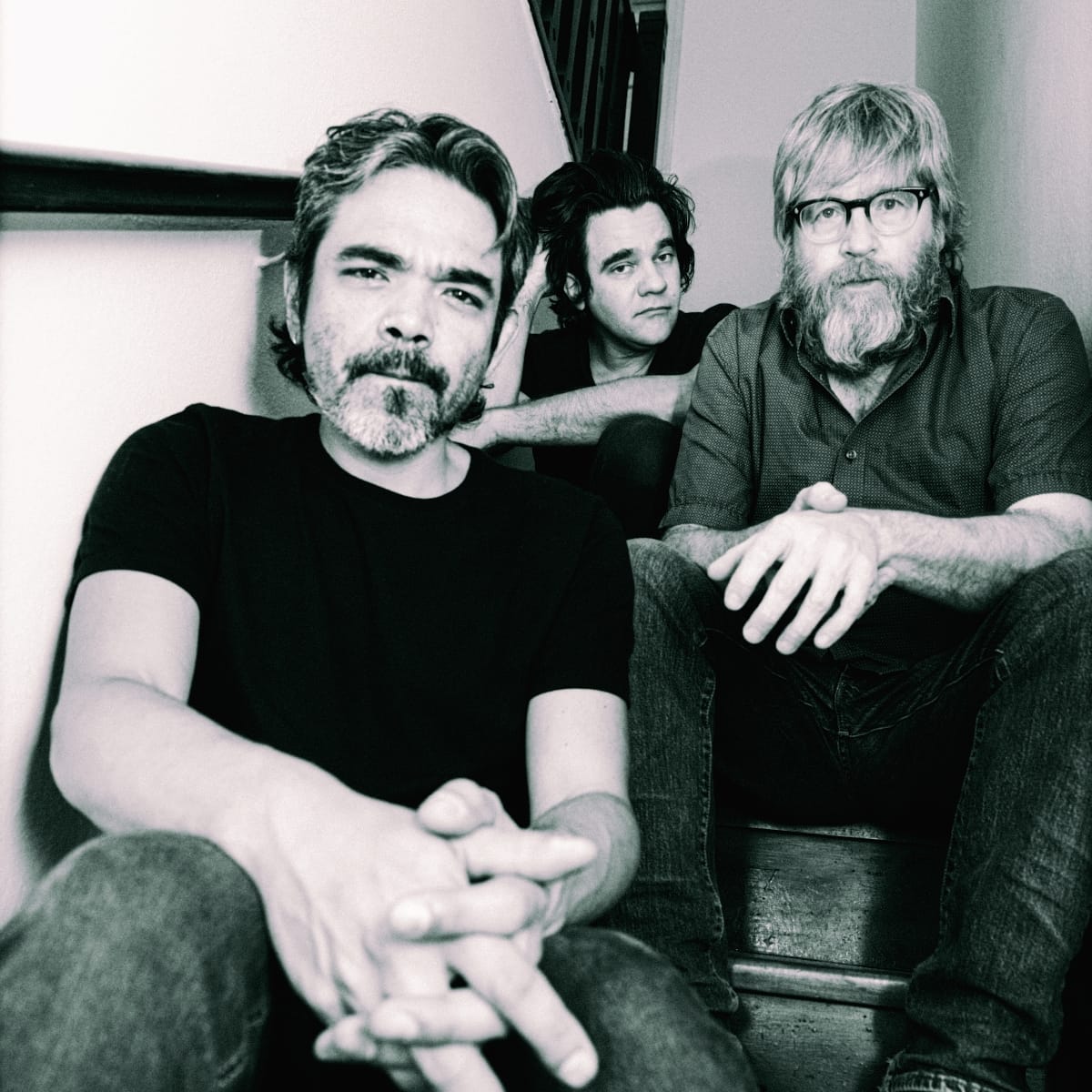 Riviera Gaz seated on a staircase in black and white — Paulo Kishimoto leaning forward with hands clasped, Gustavo Riviera behind him, Steve Shelley at right with arms over his knees.