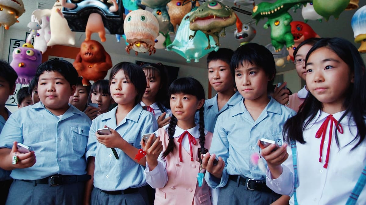 Schoolchildren in pale blue uniforms hold small handheld devices, looking upward as dozens of creatures crowd the air above them.