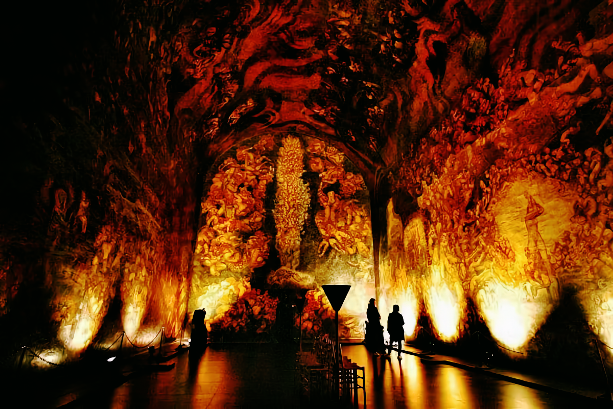 Emanuel Vigeland's windowless mausoleum: walls and vaulted ceiling wholly covered by Vita, a fresco of entangled human figures glowing amber in near-darkness, two visitors tiny against it.