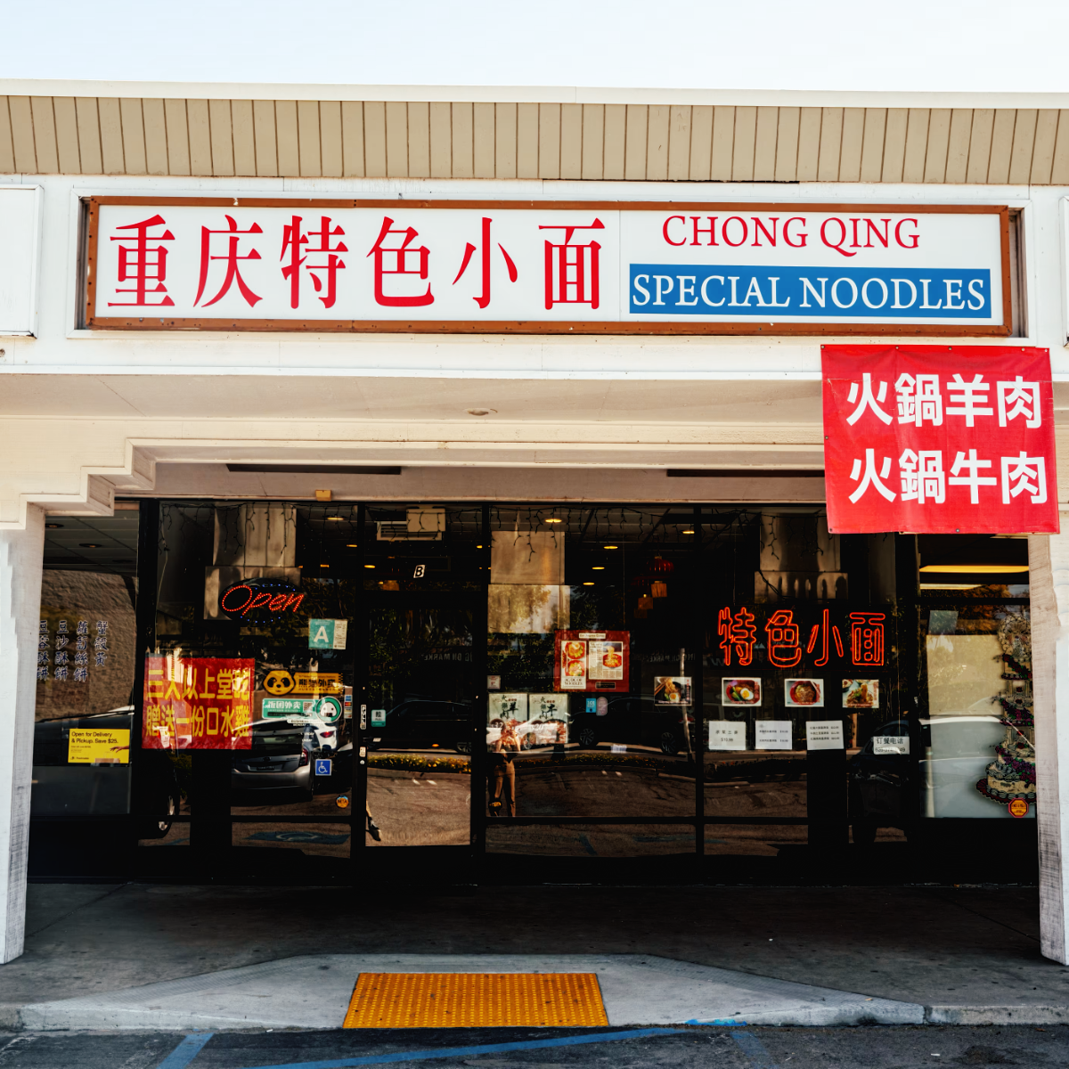 Storefront of Chong Qing Special Noodles in a strip mall, its sign in red Chinese characters and English, with a red hot-pot banner above the entrance and a neon Open sign in the dark glass.