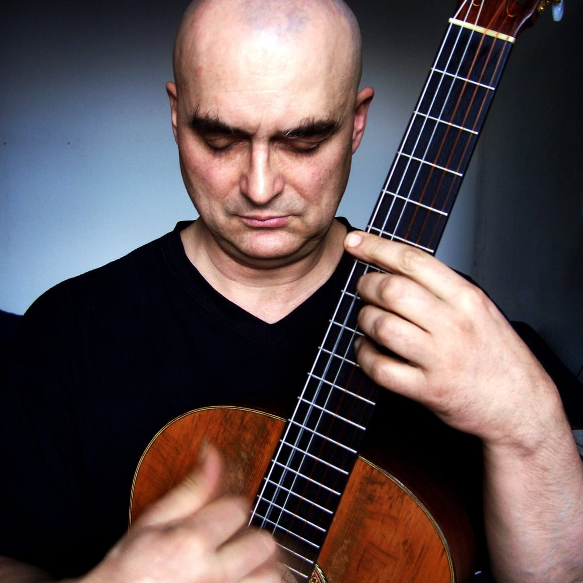 Olaf Rupp plays a nylon-string acoustic guitar held upright against his chest, eyes closed and head lowered, his picking hand blurred with motion.