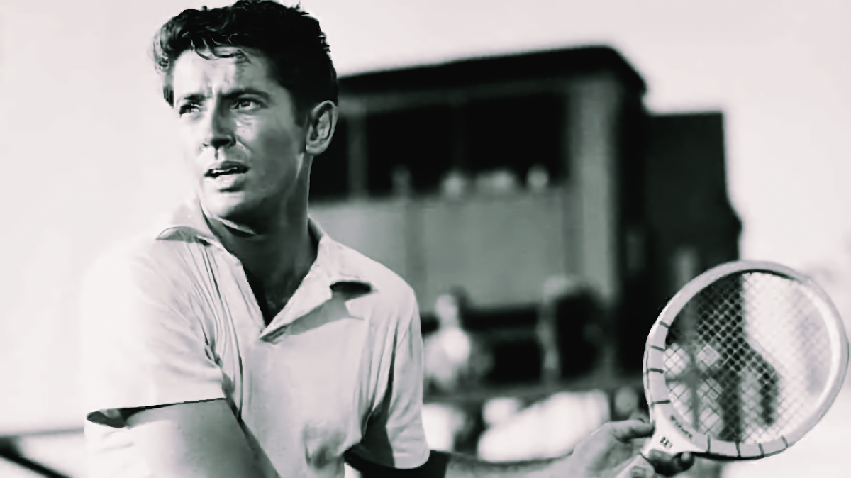 Black-and-white still from Alfred Hitchcock's Strangers on a Train: Farley Granger as tennis pro Guy Haines, racket raised mid-match, eyes on the ball, an umpire's stand blurred behind him.