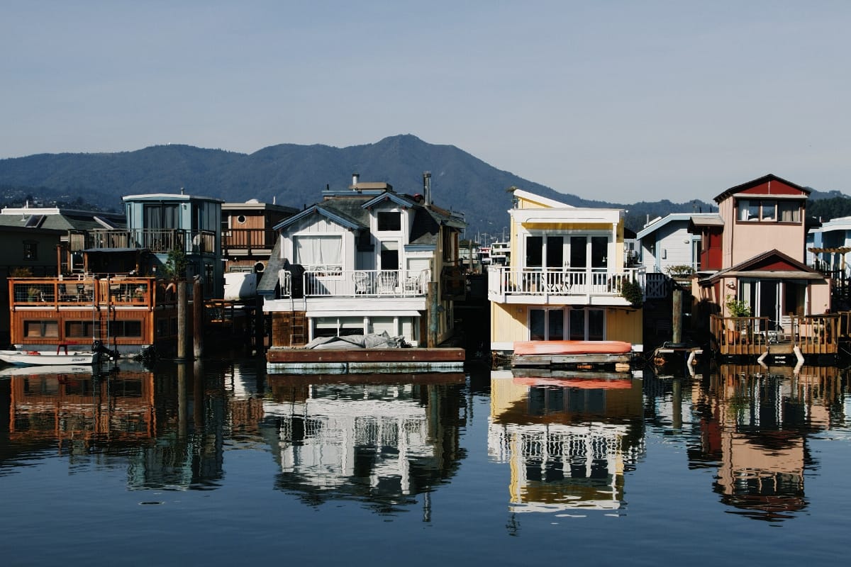 Colorful Sausalito houseboats reflect in still water, with Mount Tamalpais rising behind them under a pale sky.