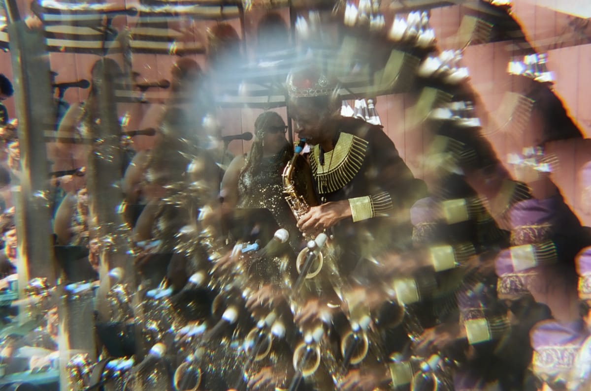 A Sun Ra Arkestra saxophonist in a jeweled crown and gold-collared robe plays at Union Pool, the scene multiplied and fractured through a prism lens.